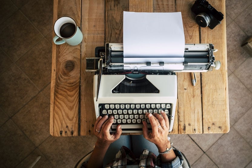 Someone using an old fashioned typewriter on a wooden table.