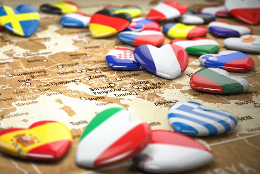 A lot of heart-shaped badges with various world country flags emblazoned on them lying across a world map.
