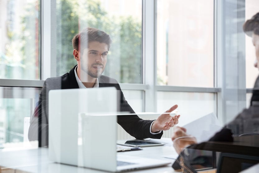 Two men sitting across the table from each other discussing something with a laptop open on the table.